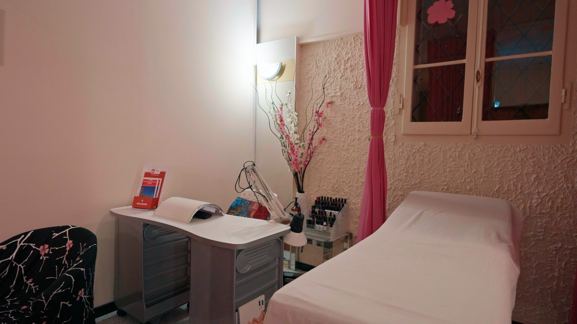 Una cabina di Estetica Aries pronta per un trattamento: il lettino, la lampada e la tenda rosa.